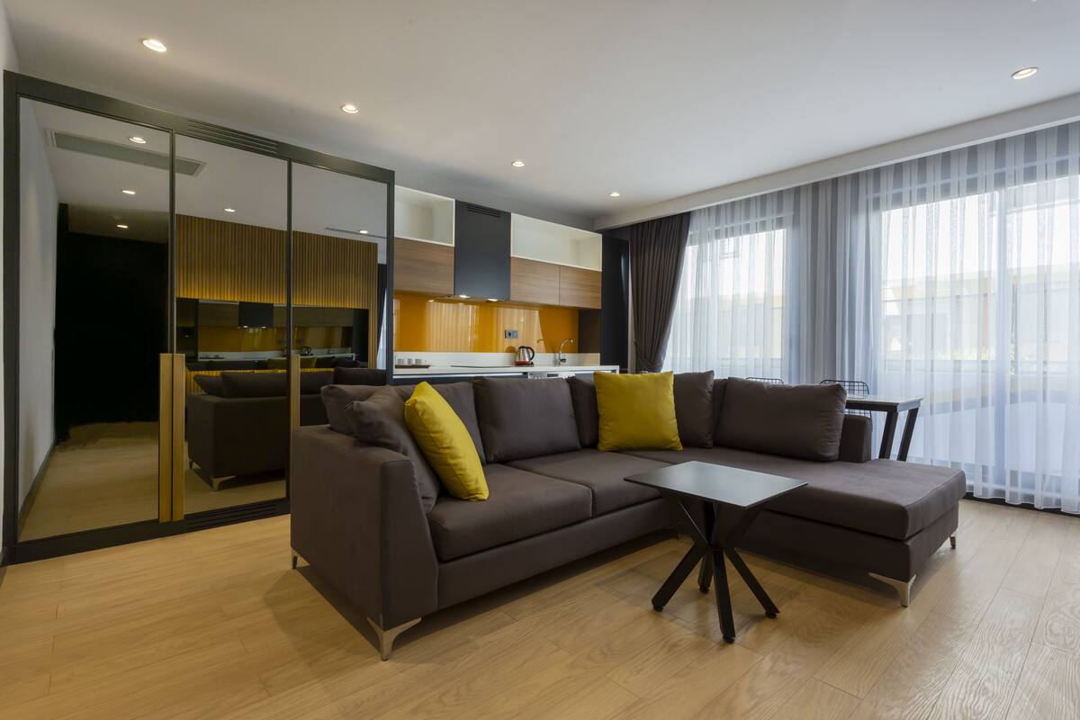 A modern living room with a brown sofa, a small table, and a kitchen in the background.