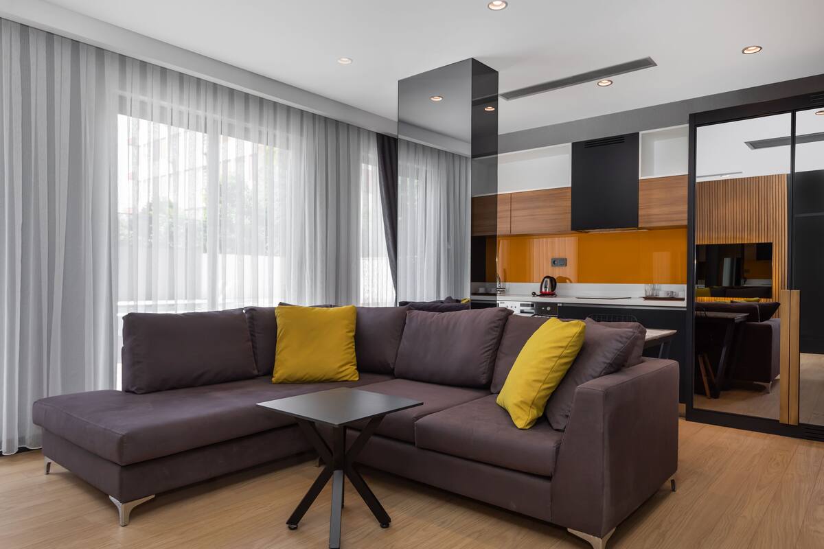 A modern living room with a sectional sofa, a small table, and a kitchen area visible through an open door.