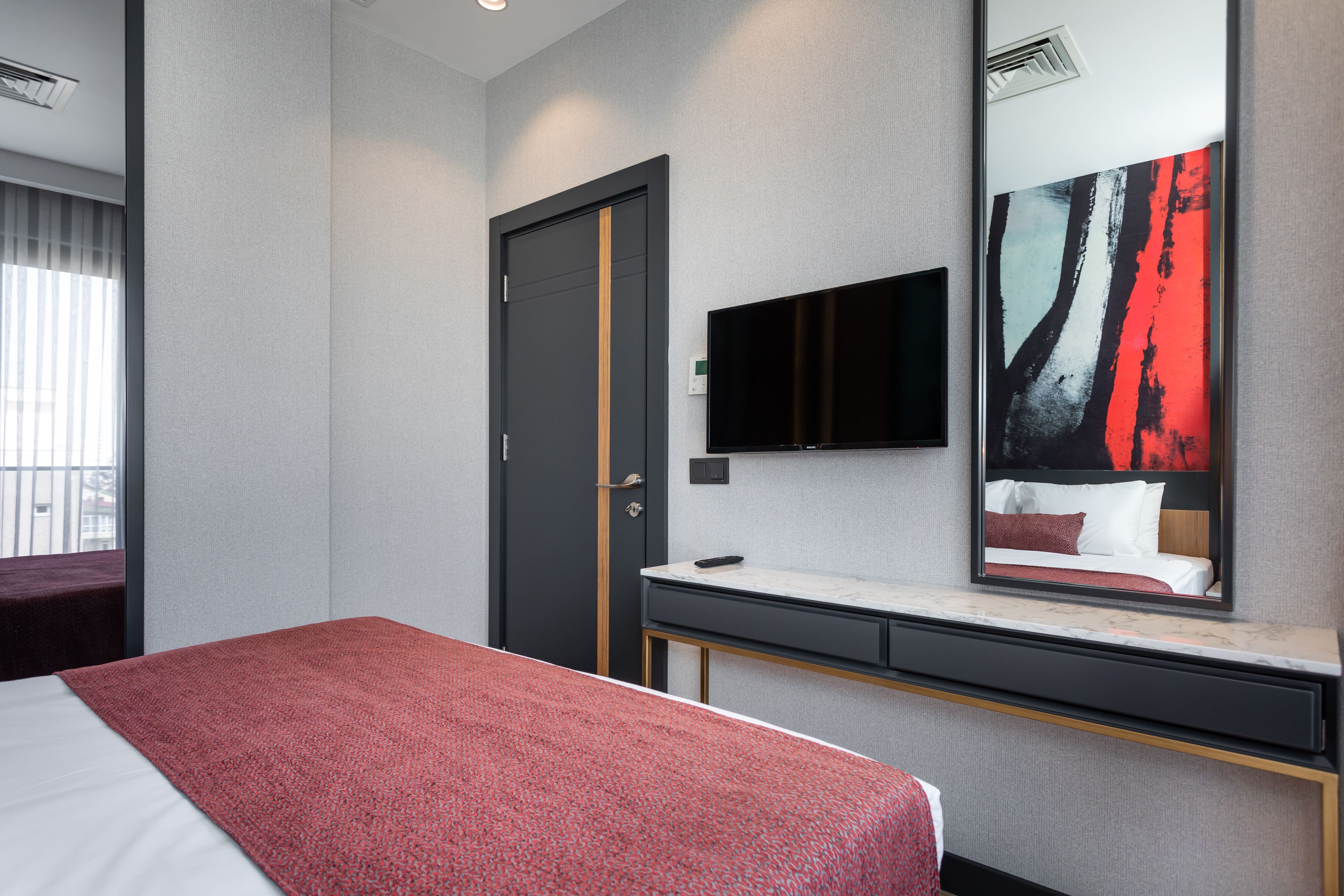 Een hotelkamer met een bed, een bureau, een televisie en een grote spiegel.