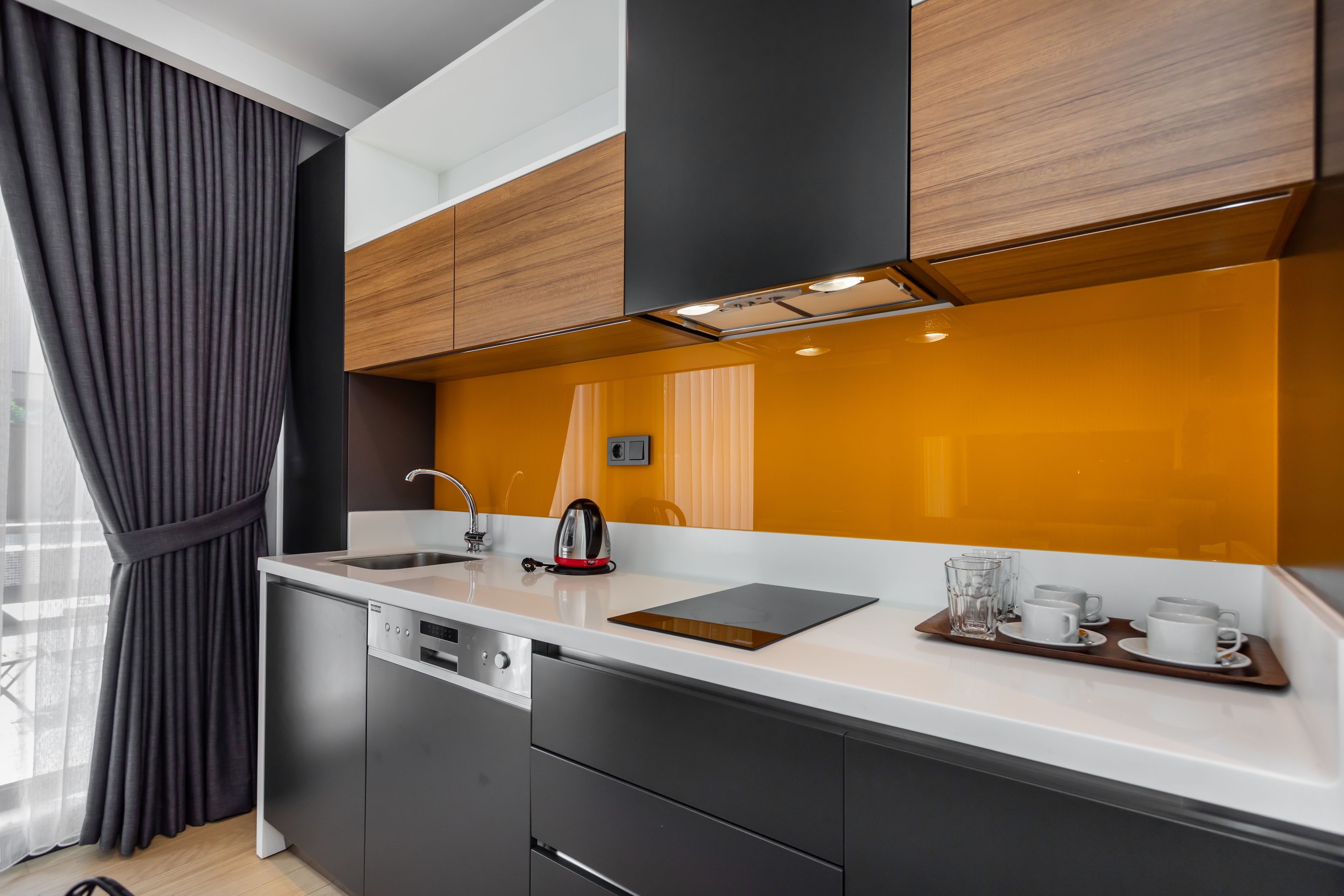 A modern kitchen with dark cabinets, a white countertop, and a stainless steel kettle.