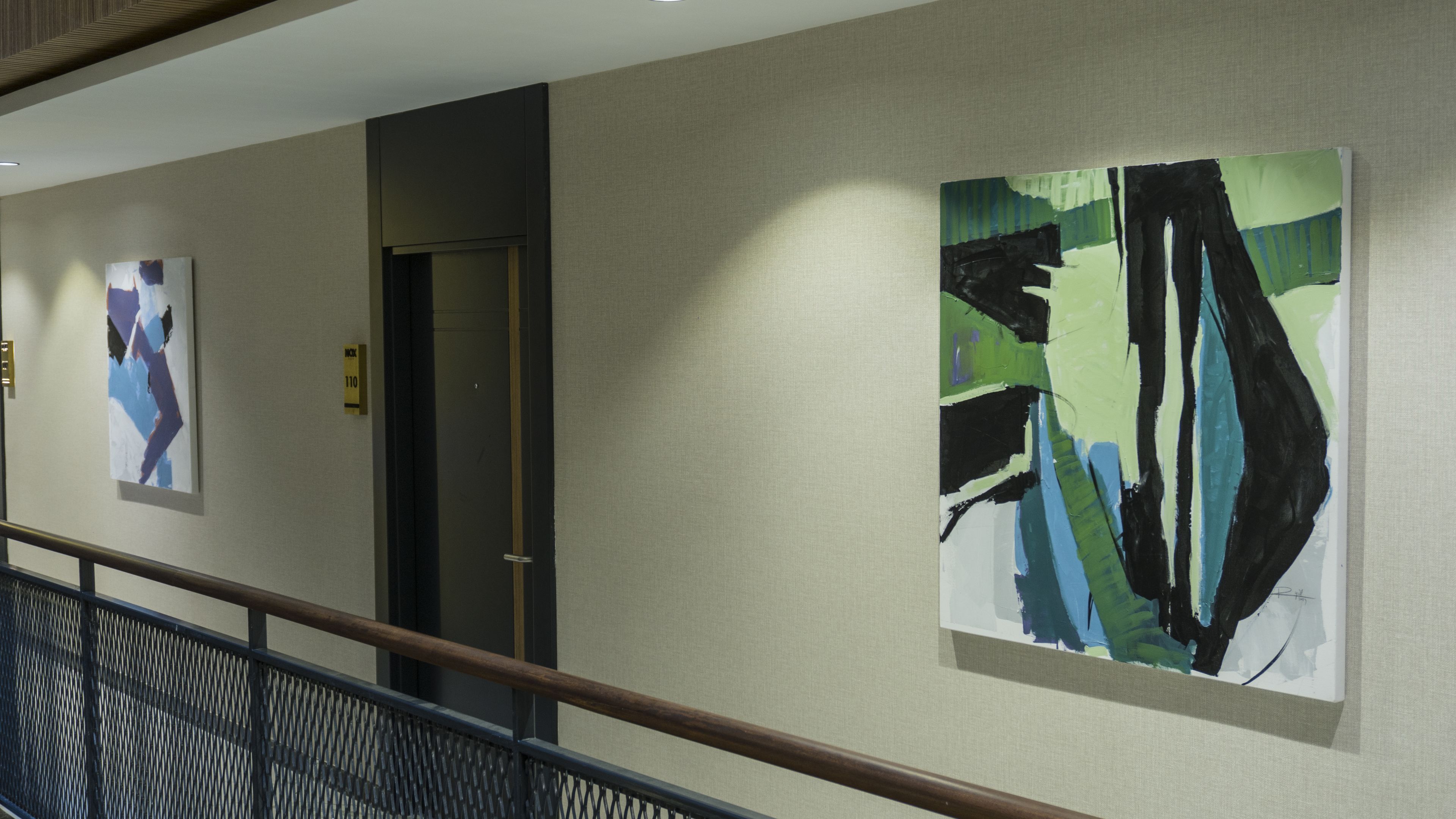 Un couloir orné d’œuvres d’art abstraites, une porte et une rampe d’escalier.