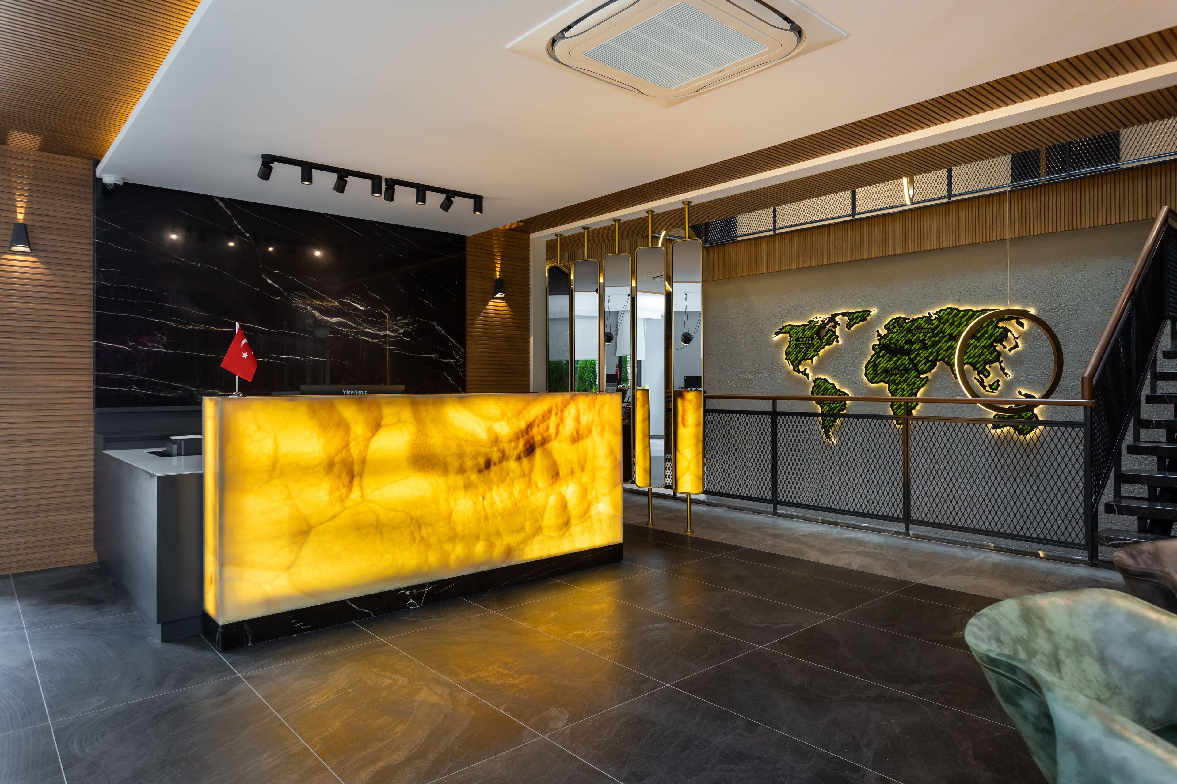 A modern reception area with a marble reception desk, a world map mural, and a staircase.