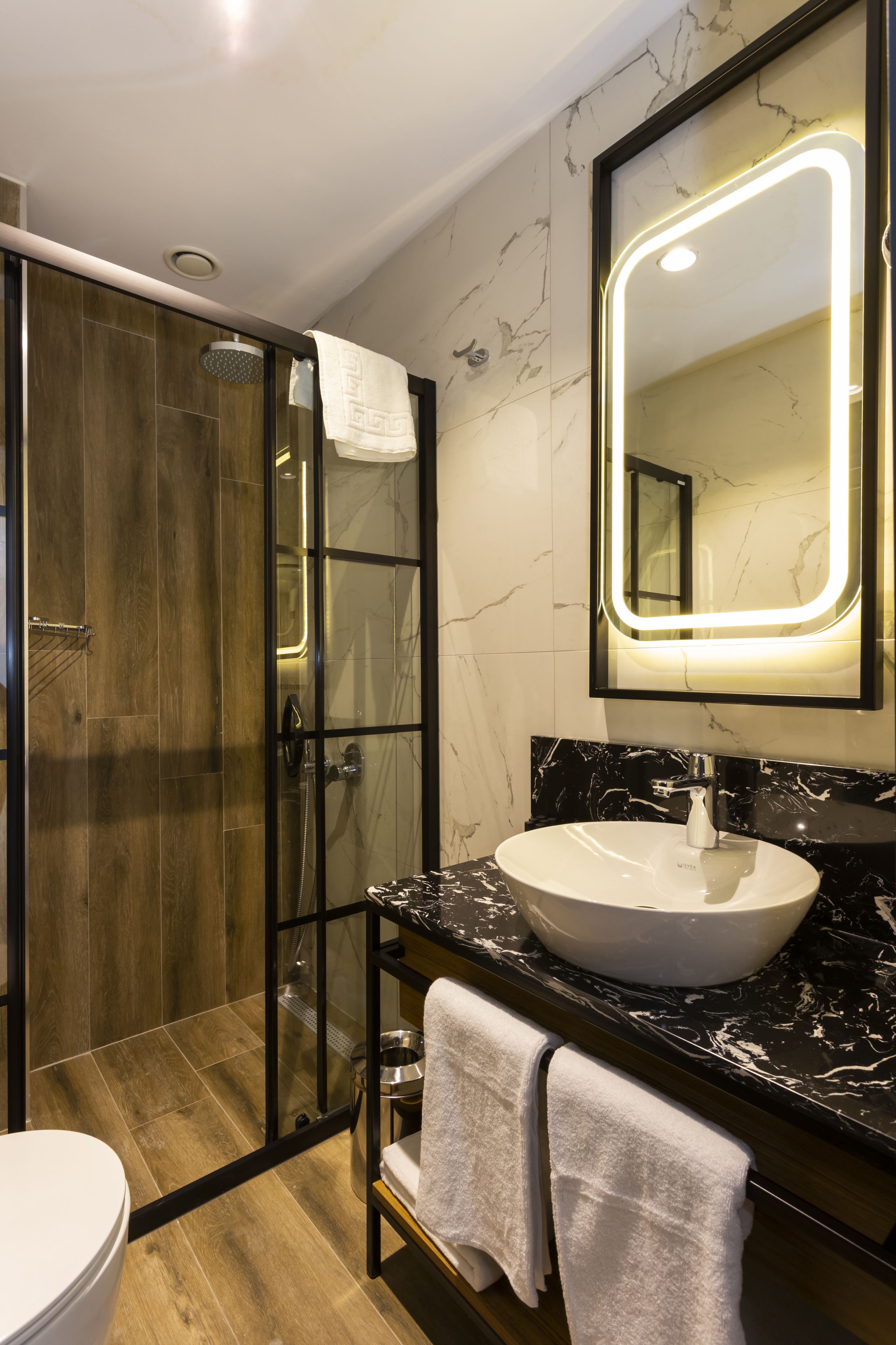 A modern bathroom with a glass-enclosed shower, a white sink, and a large mirror with LED lighting.
