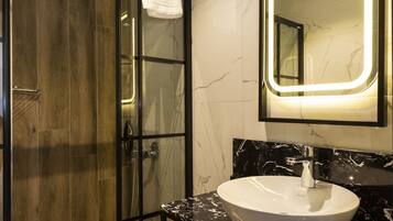 A modern bathroom with a glass-enclosed shower, a white sink, and a large mirror with LED lighting.