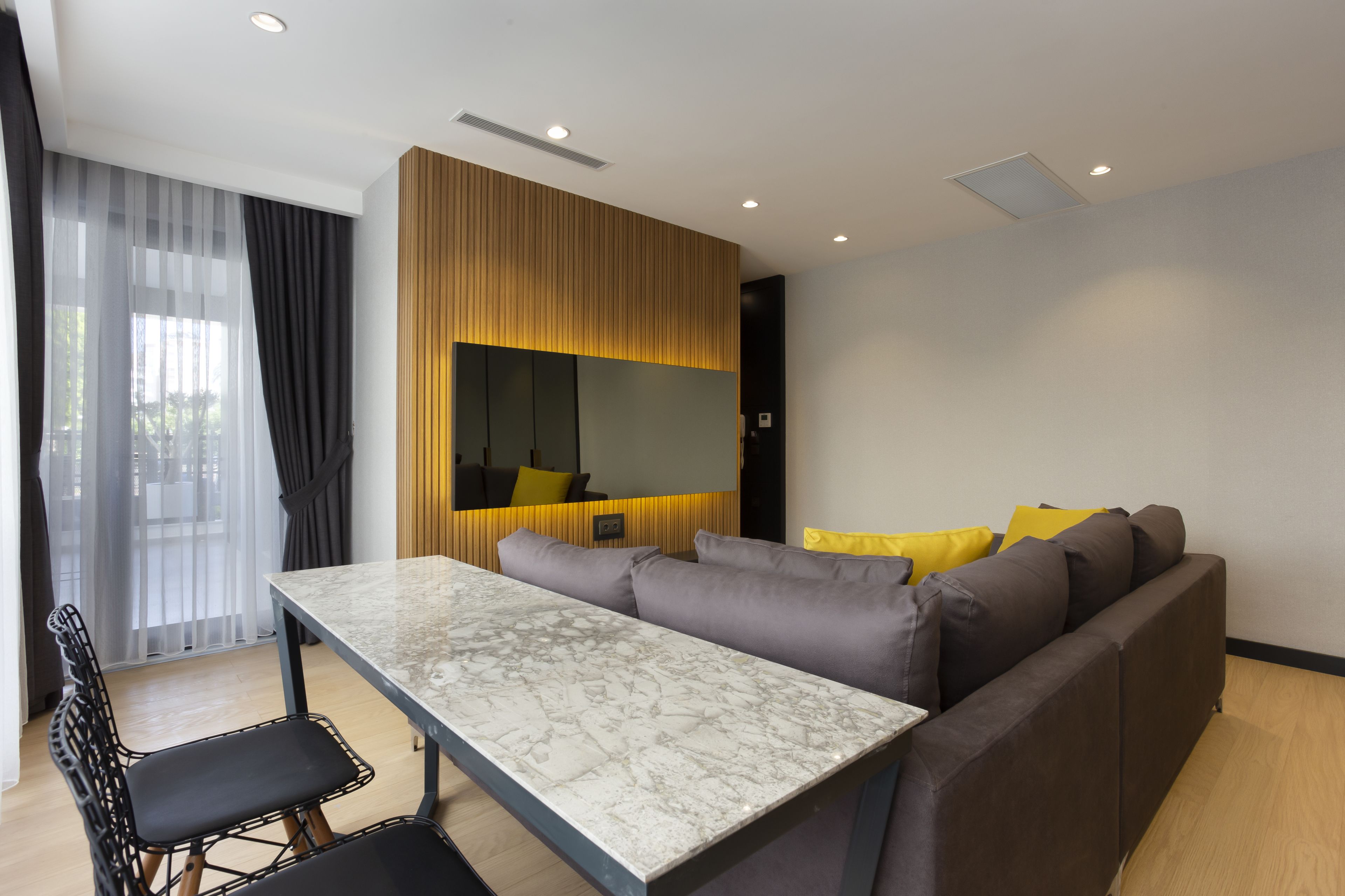 A modern living room with a marble table, grey sofa, and yellow cushions.