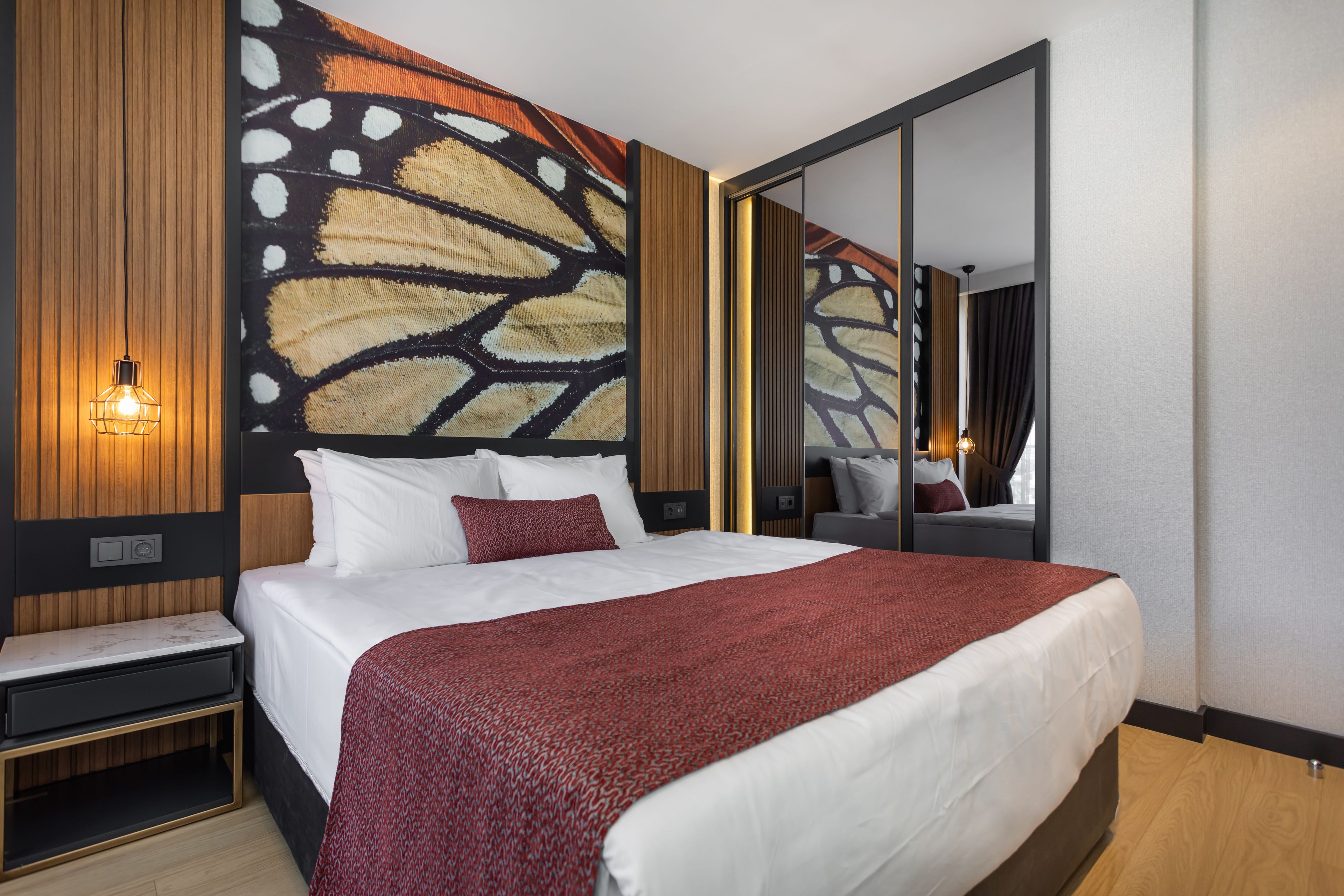 A modern hotel room with a large bed, a wooden headboard, a wall-mounted light, and a large mirror.