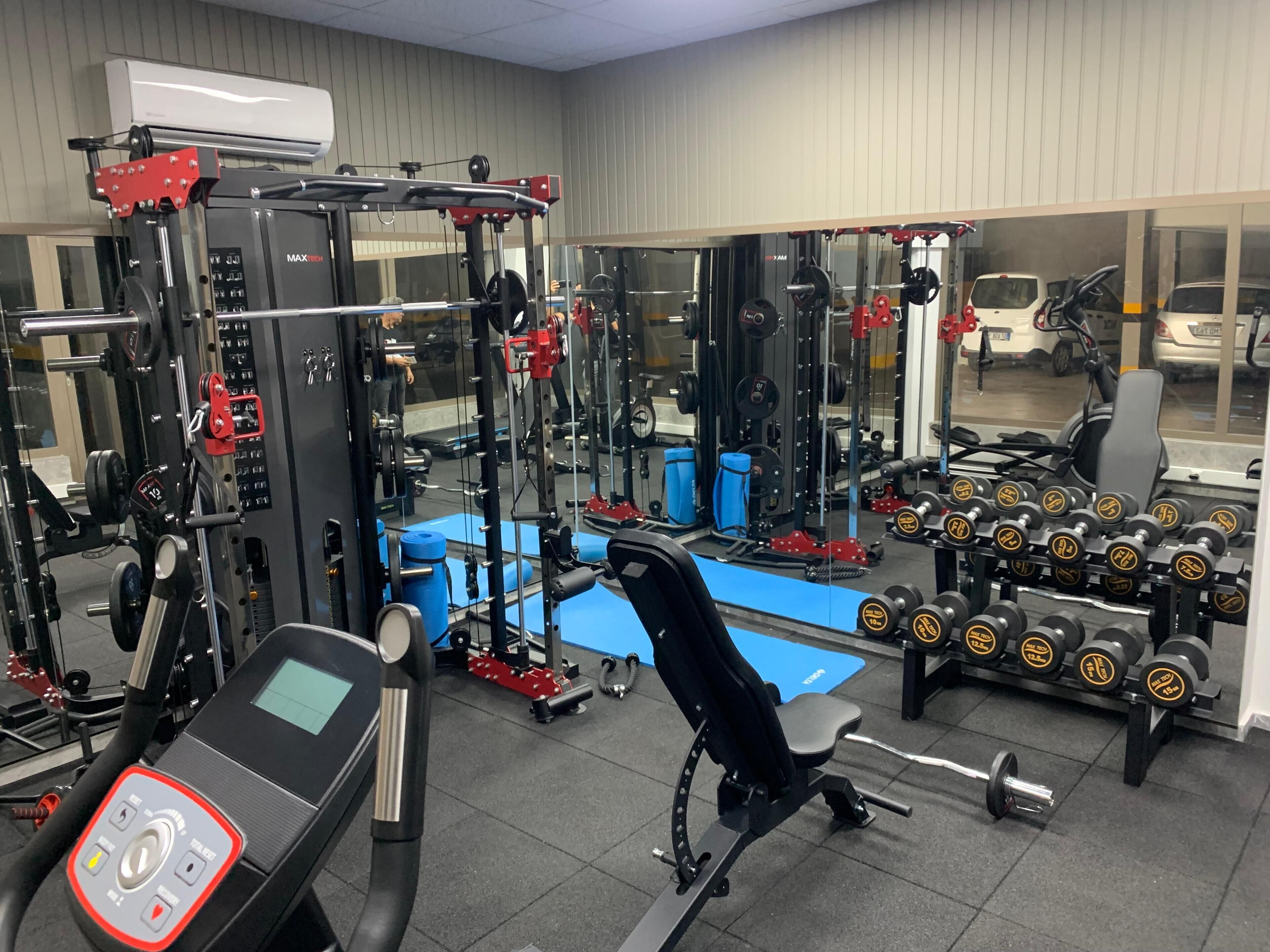 Een fitnessruimte met diverse trainingsapparaten, waaronder een loopband, krachtapparaten en een bankdrukapparaat.