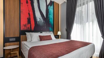 Een moderne hotelkamer met een groot bed, een klein nachtkastje, een kunstwerk aan de muur en een raam met gordijnen.