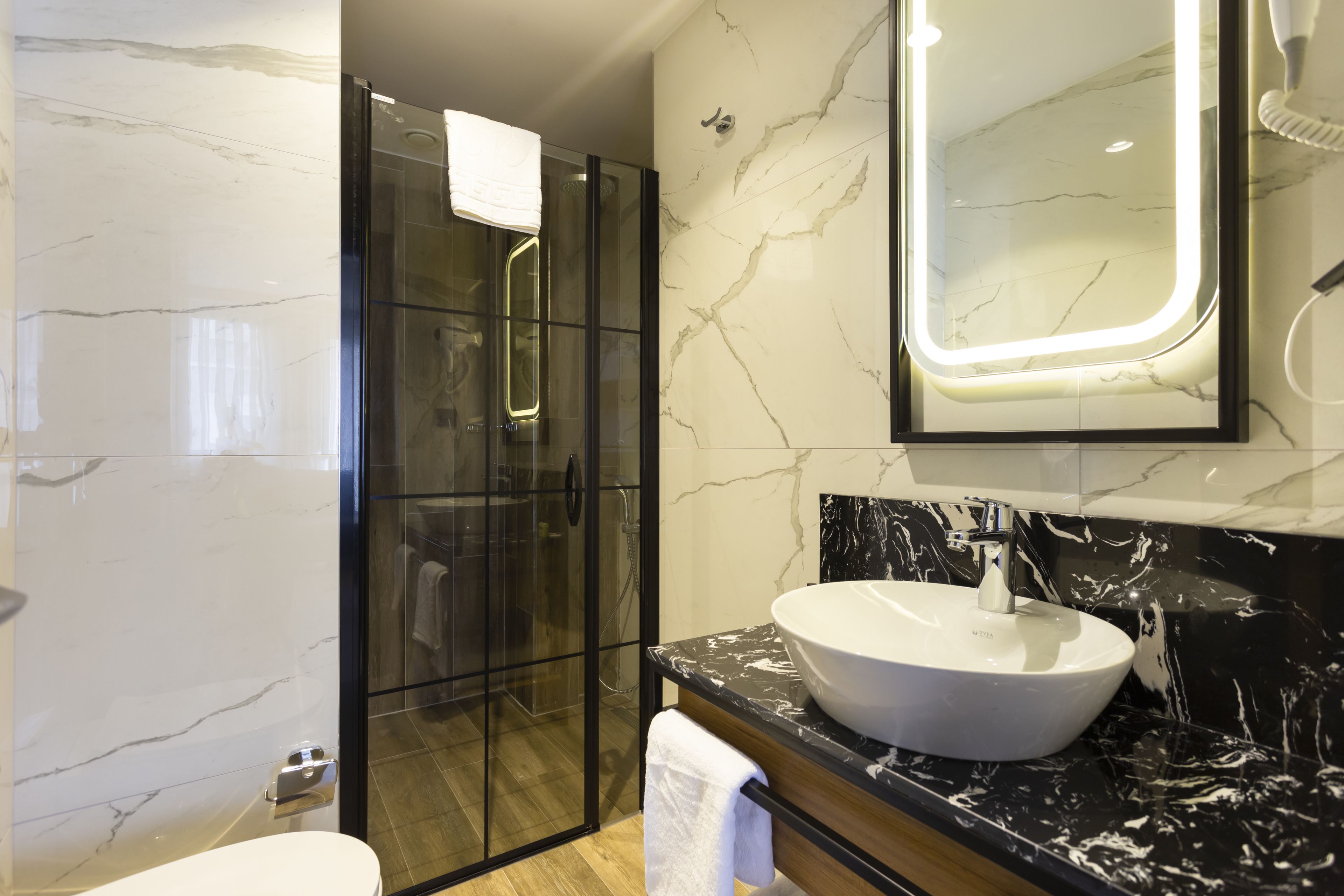 A modern bathroom with a glass-enclosed shower, a white sink, and a marble-tiled wall.