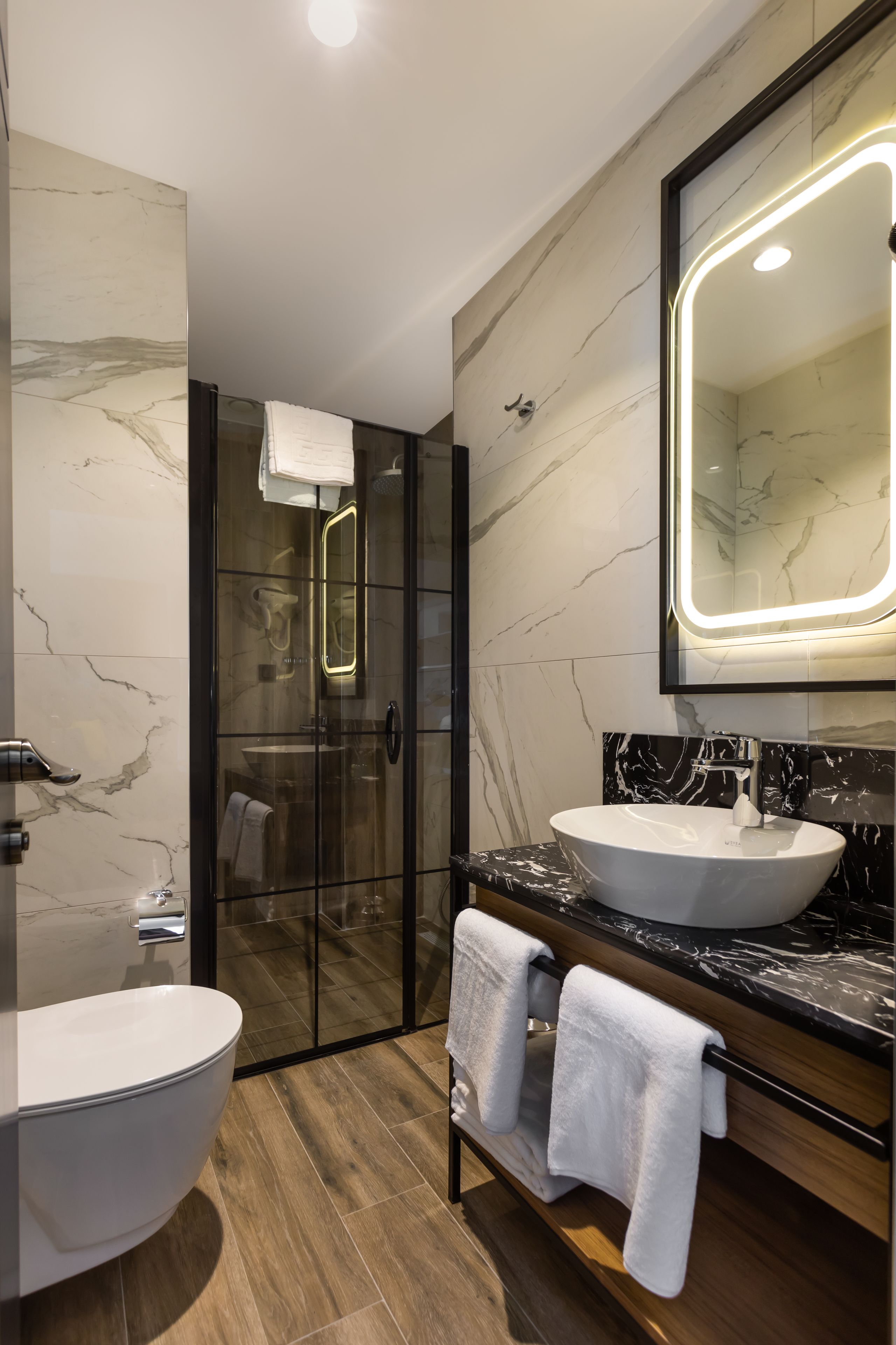 A modern bathroom with a glass-enclosed shower, two sinks, and a large mirror with integrated lighting.