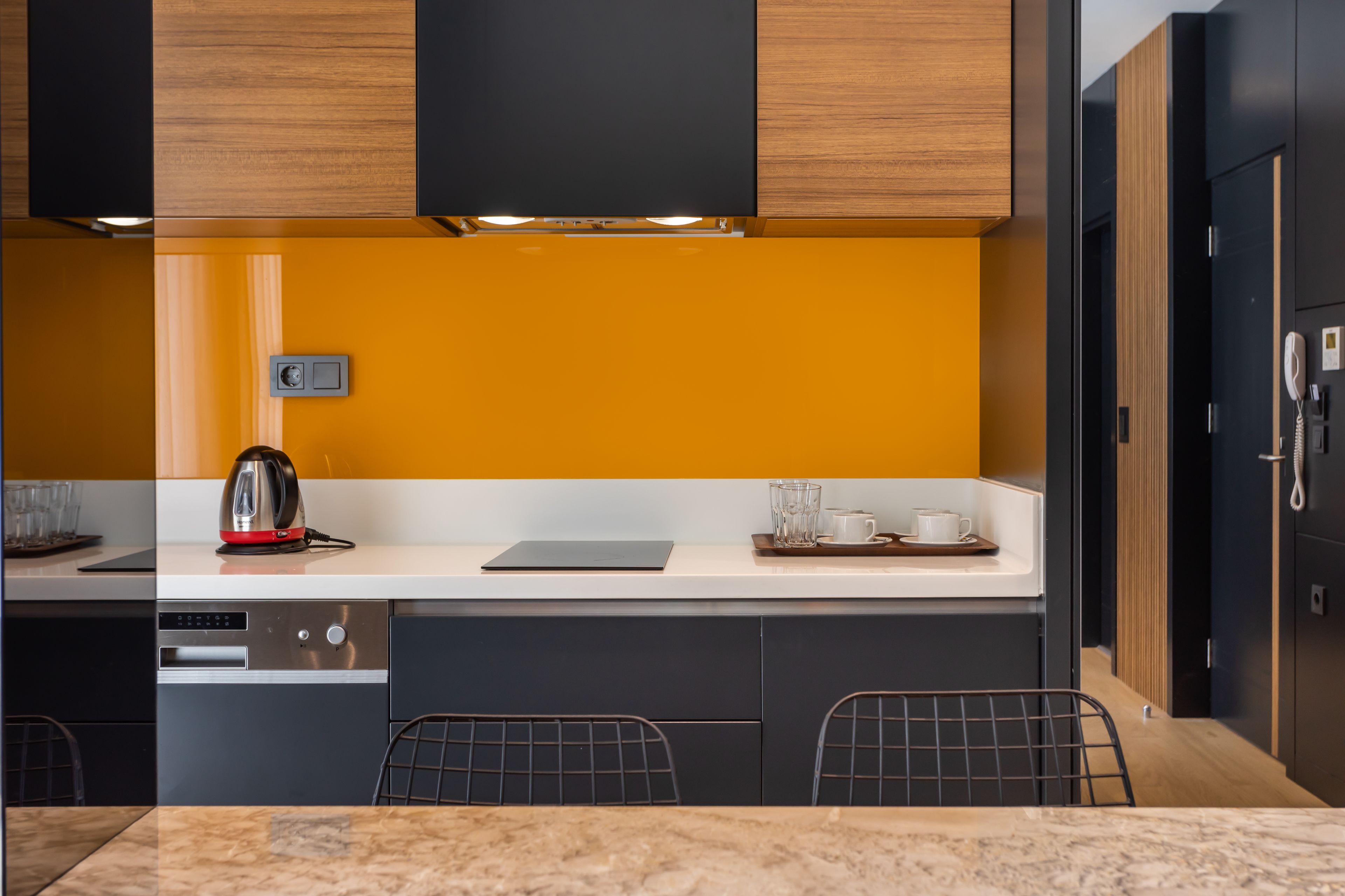 A modern kitchen with black cabinets, a white countertop, and a yellow accent wall.