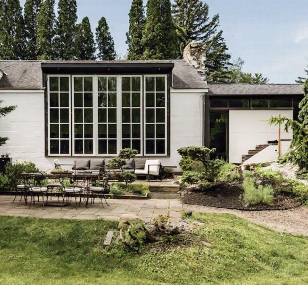 A modern house with a large window, outdoor seating, and a well-maintained garden.