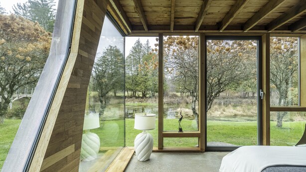 Un dormitorio con un ventanal grande, una cama, una lámpara y vistas a un parque.