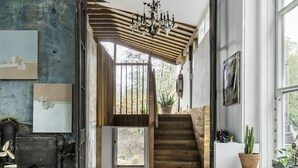 Un interior moderno con una escalera que conduce a un balcón, una araña y un escritorio de madera rústica.