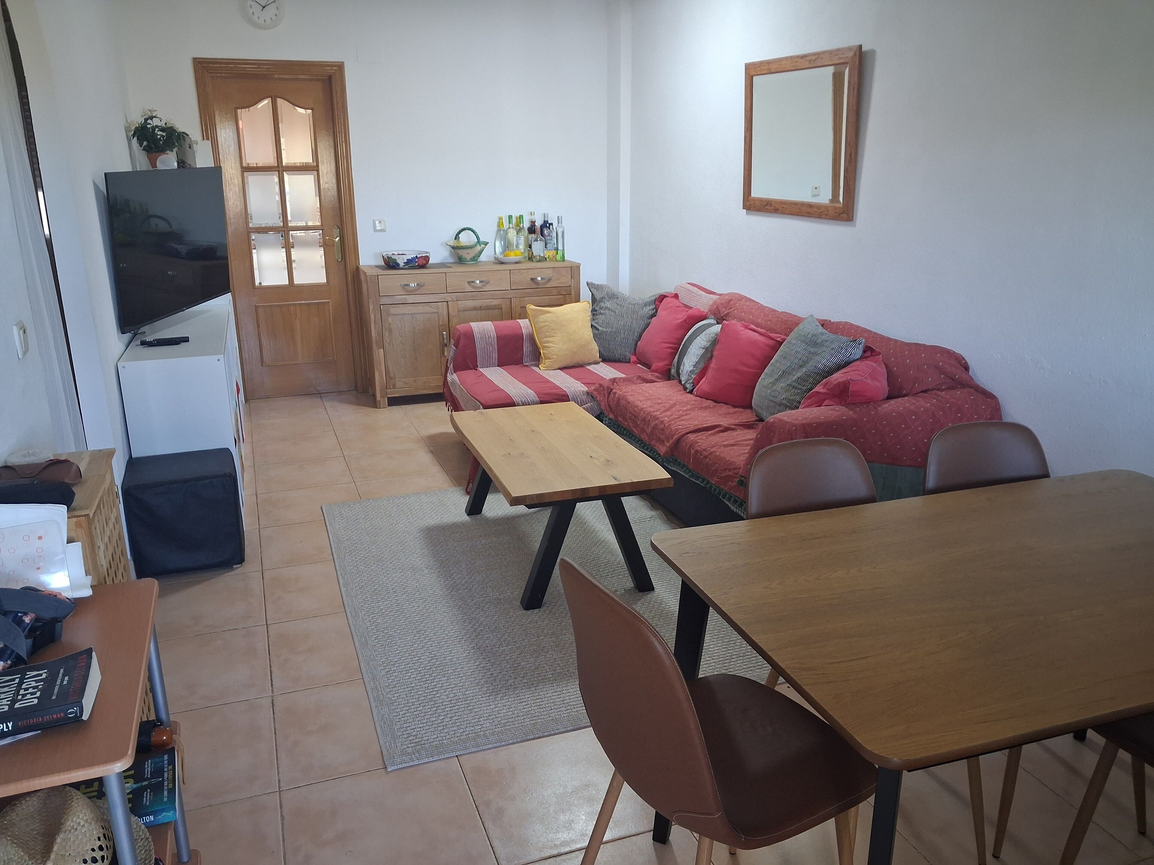 Ein Wohnzimmer mit Sofa, Couchtisch und Fernseher. Es gibt einen Holzschrank und einen kleinen Tisch mit Stühlen.