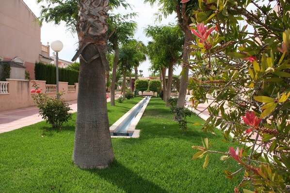 A well-maintained garden with a central water feature, surrounded by neatly trimmed grass and various trees.