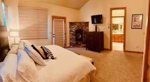 A bedroom with a bed, a stone fireplace, a television, and a bathroom visible through an open door.