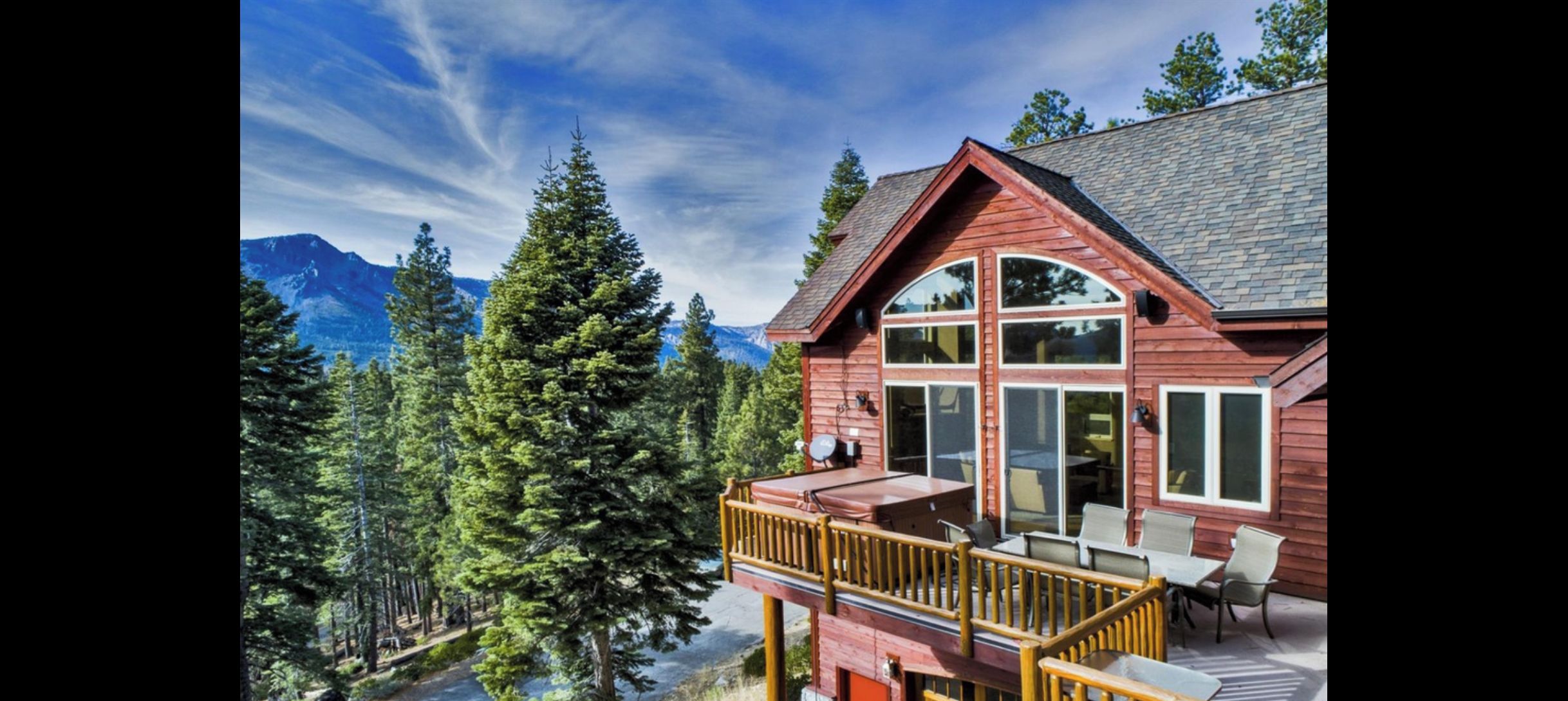 Une cabane en bois dotée d’une terrasse, de grandes fenêtres et surplombant un paysage montagneux.
