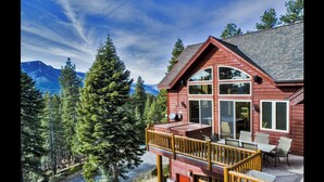 A wooden cabin with a deck, large windows, and a mountain backdrop.