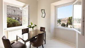 A dining area with a table and chairs, a vase with flowers, and a view of a building through large windows. - Amazing Colosseo (Rome)