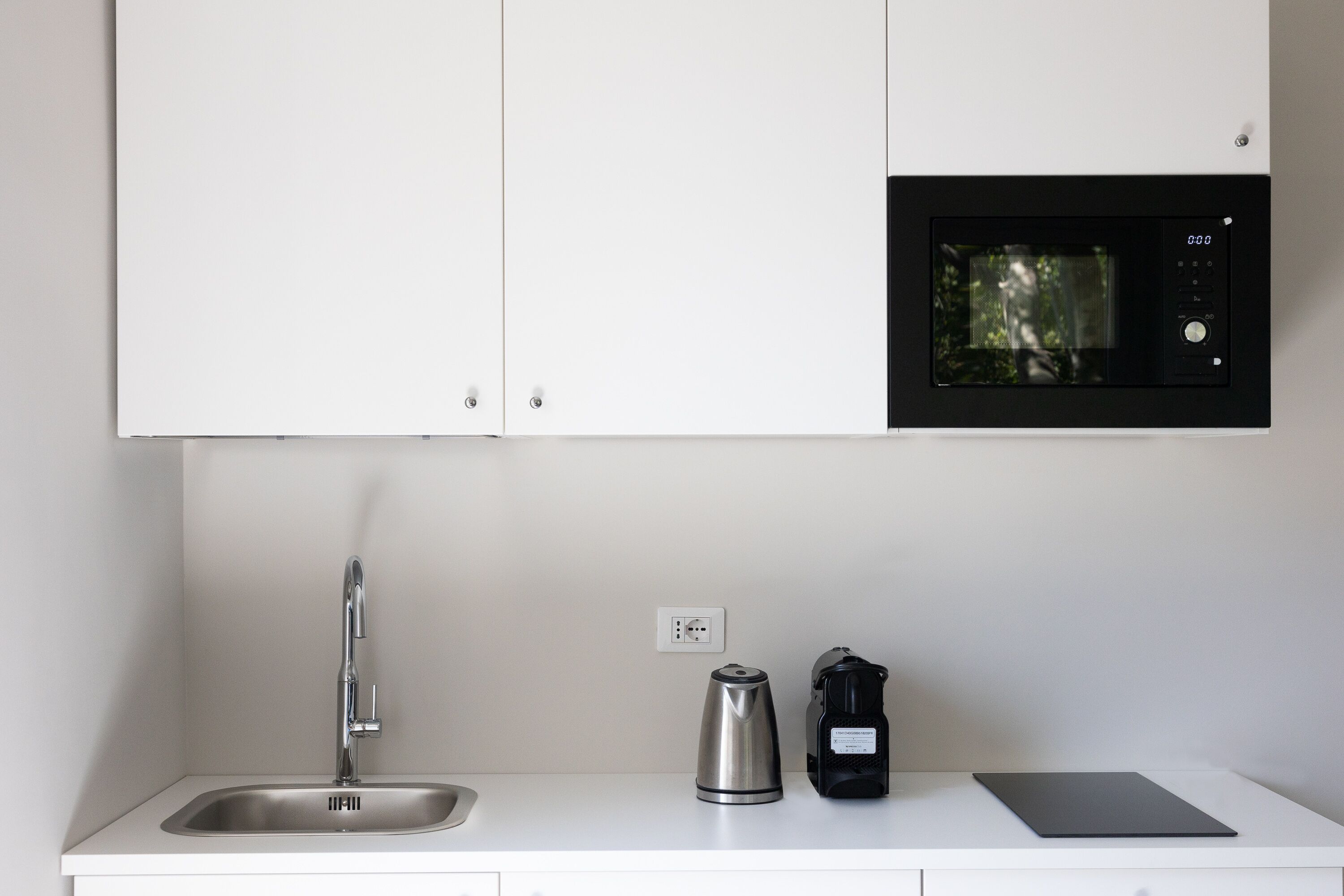 A kitchen with a stainless steel sink, a kettle, a coffee maker, and a microwave.