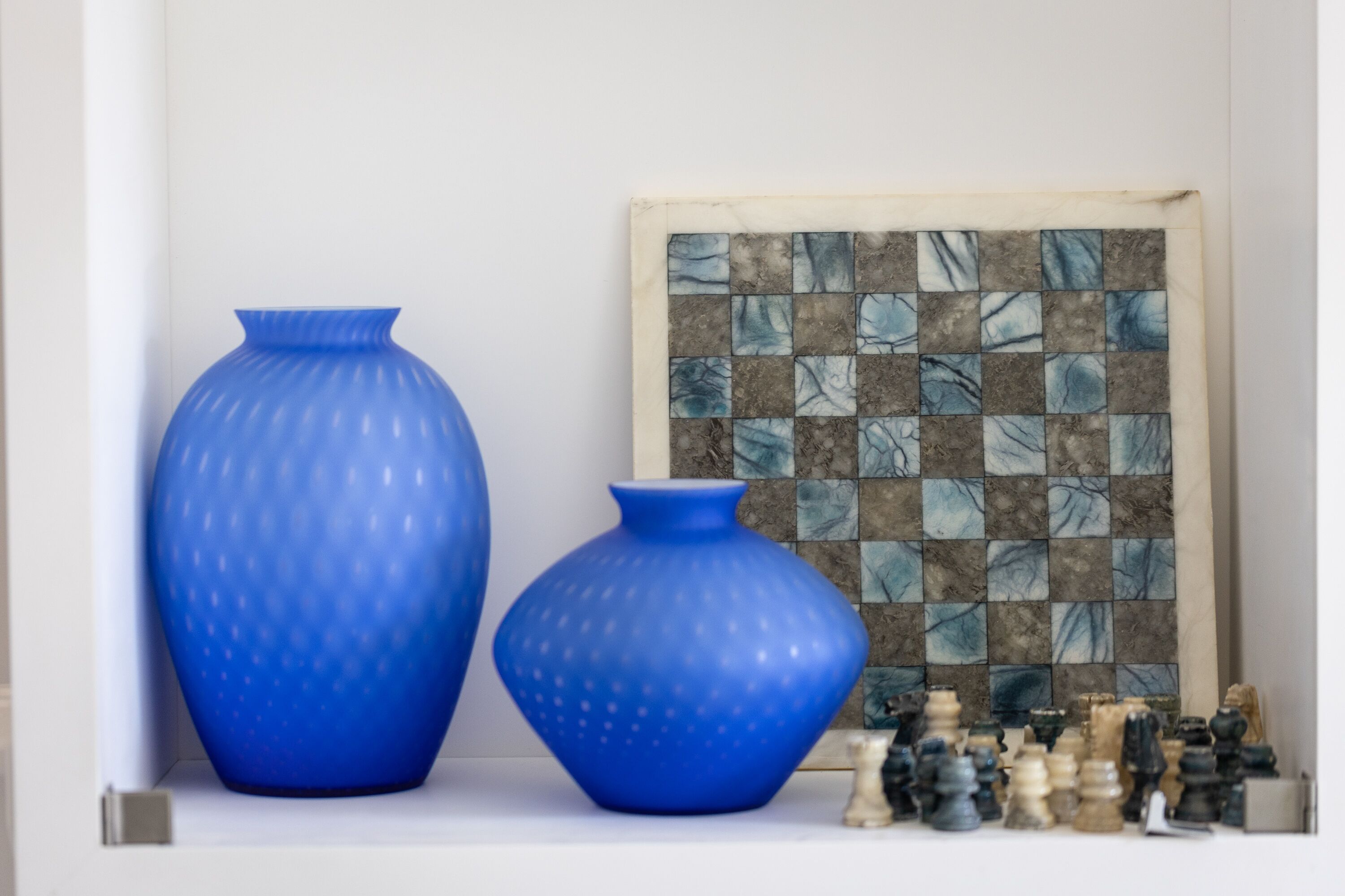 Dos jarrones azules sobre una estantería con un juego de ajedrez y un muro de mosaicos.