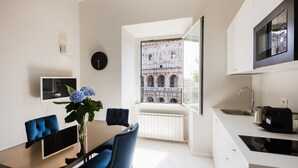 A modern kitchen with a large window, a dining area with blue chairs, and a built-in TV. - Amazing Colosseo (Rome)