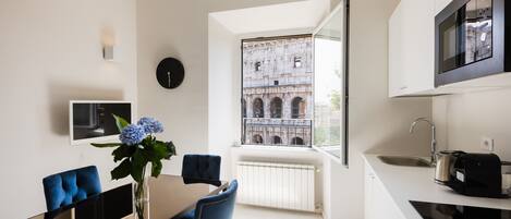 A modern kitchen with a large window, a dining area with blue chairs, and a built-in TV.