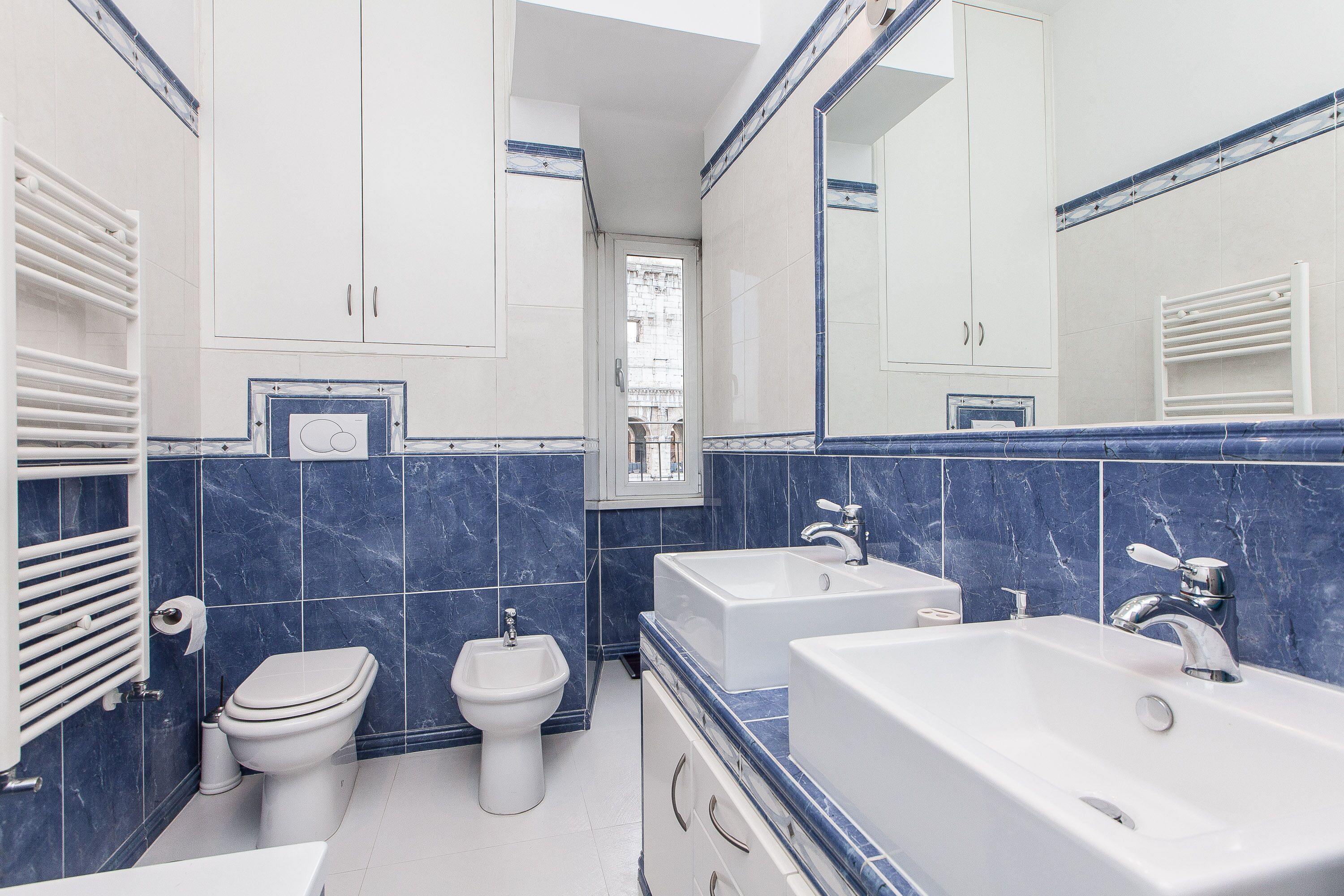 Een moderne badkamer met toilet, bidet en twee wastafels.
