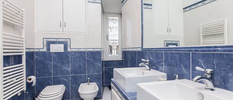 Een moderne badkamer met toilet, bidet en twee wastafels.
