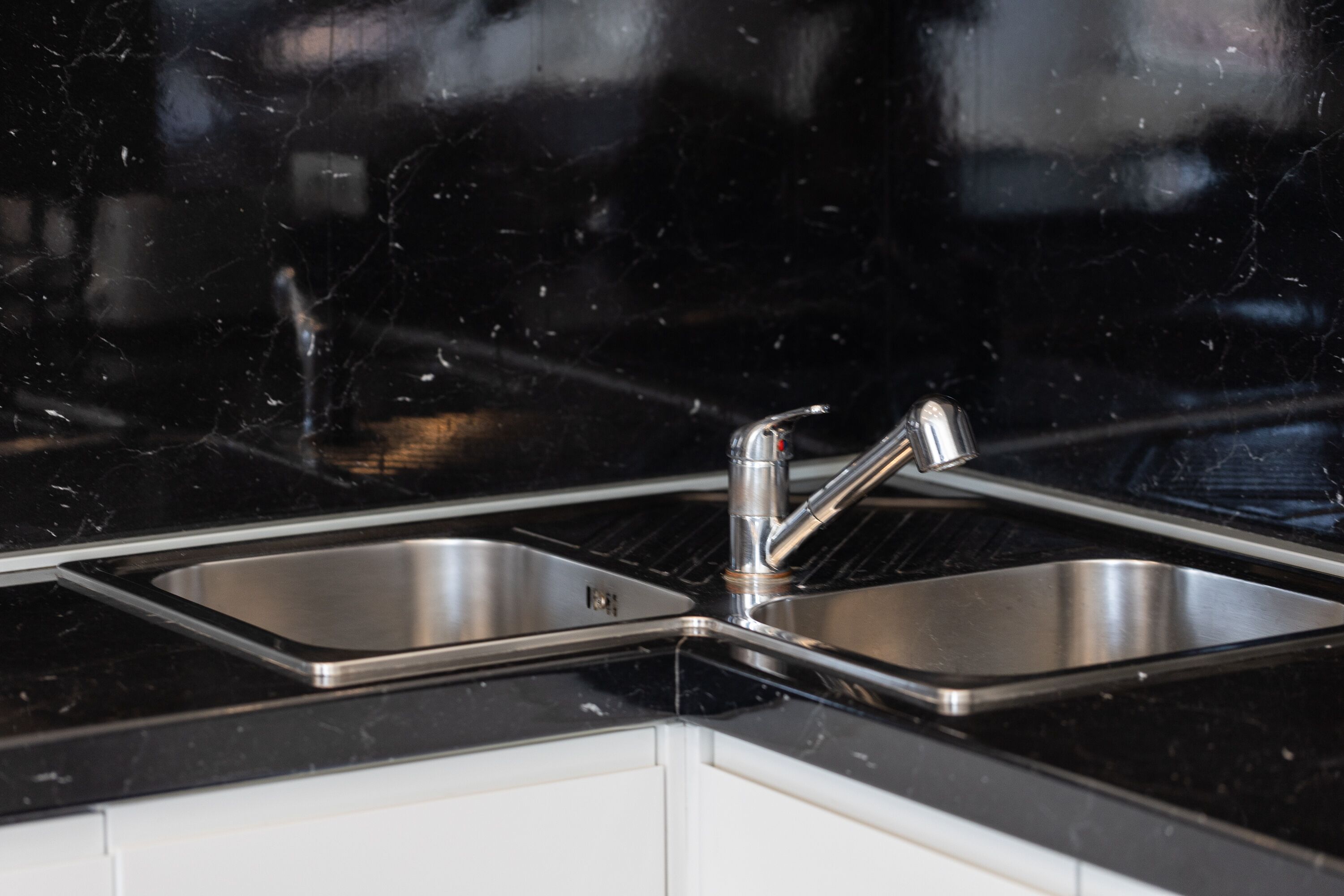 A kitchen with two stainless steel sinks and a black countertop.