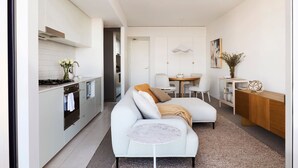 A modern kitchen with white cabinets, a stove, and a sink. There is a dining area with a table and chairs. A sofa is placed in the living area. - Sky Pad by Contemporary Hotels (DARLINGHURST)