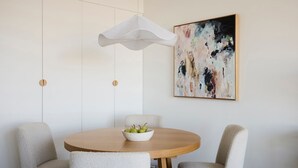 A dining area with a round wooden table, two chairs, a white bowl with pears, a white hanging light fixture, and a large abstract painting on the wall. - Sky Pad by Contemporary Hotels (DARLINGHURST)