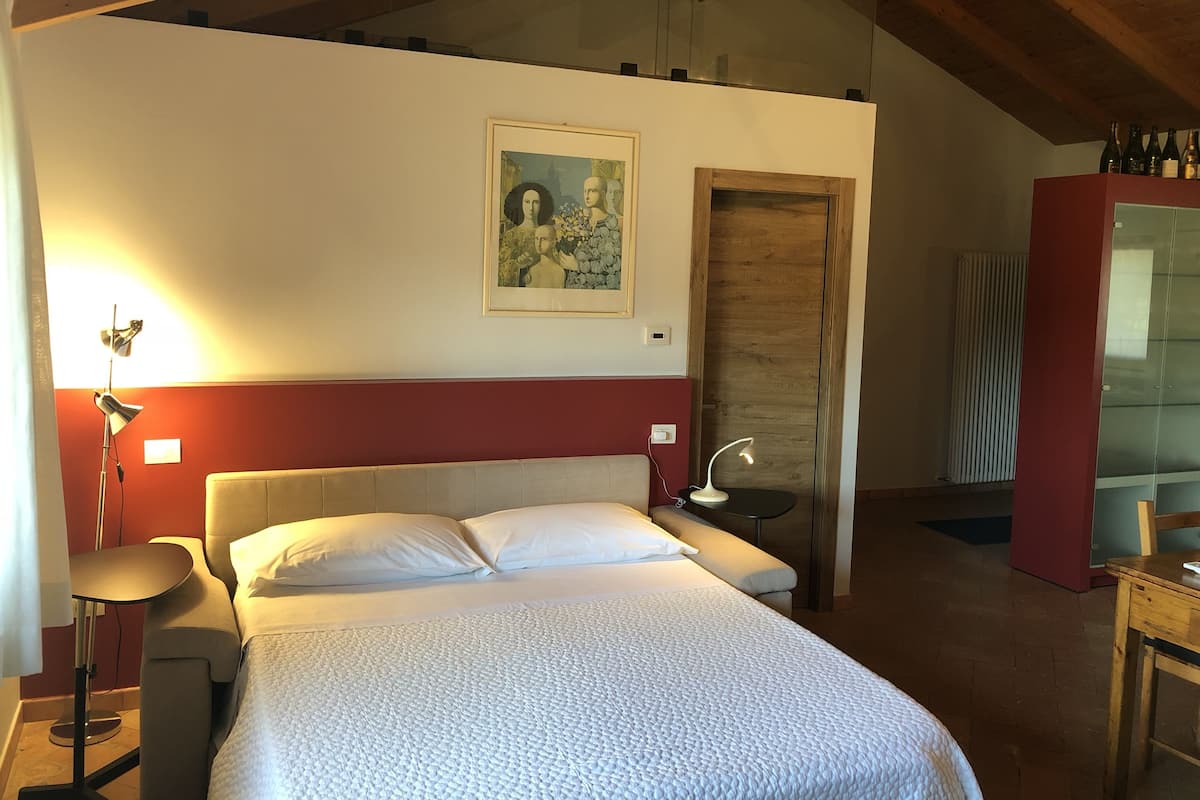 A bedroom with a bed, a bedside lamp, a painting on the wall, and a red cabinet.
