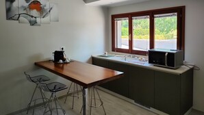 Uma cozinha moderna com uma mesa de madeira, banquetas, micro-ondas e uma janela com vista para o verde.