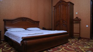Ein hölzernes Bett mit weißer Bettdecke in einem Zimmer mit gemustertem Teppich und einem Holzschrank.