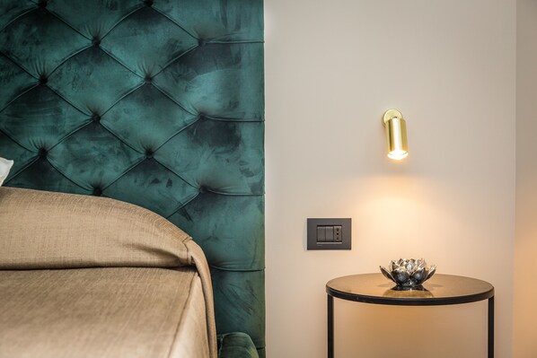 Un dormitorio con cabecera capitonada, una mesita de noche con lámpara y un interruptor de pared.