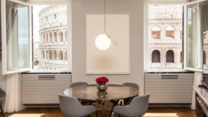 Un coin repas comprenant une table ronde, quatre chaises, un vase avec des fleurs rouges et un luminaire suspendu.