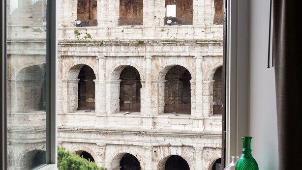 Une vue sur un arc romain antique, aperçu à travers une fenêtre, avec un vase vert posé sur le rebord de la fenêtre.