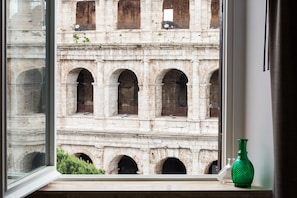 A view of an ancient Roman archway through a window, with a green vase on the windowsill. - Amazing View Colosseo (Rome)