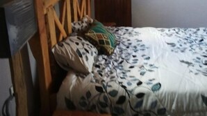 A bedroom with a wooden headboard, a bed with patterned bedding, a bedside table, and a wooden door.