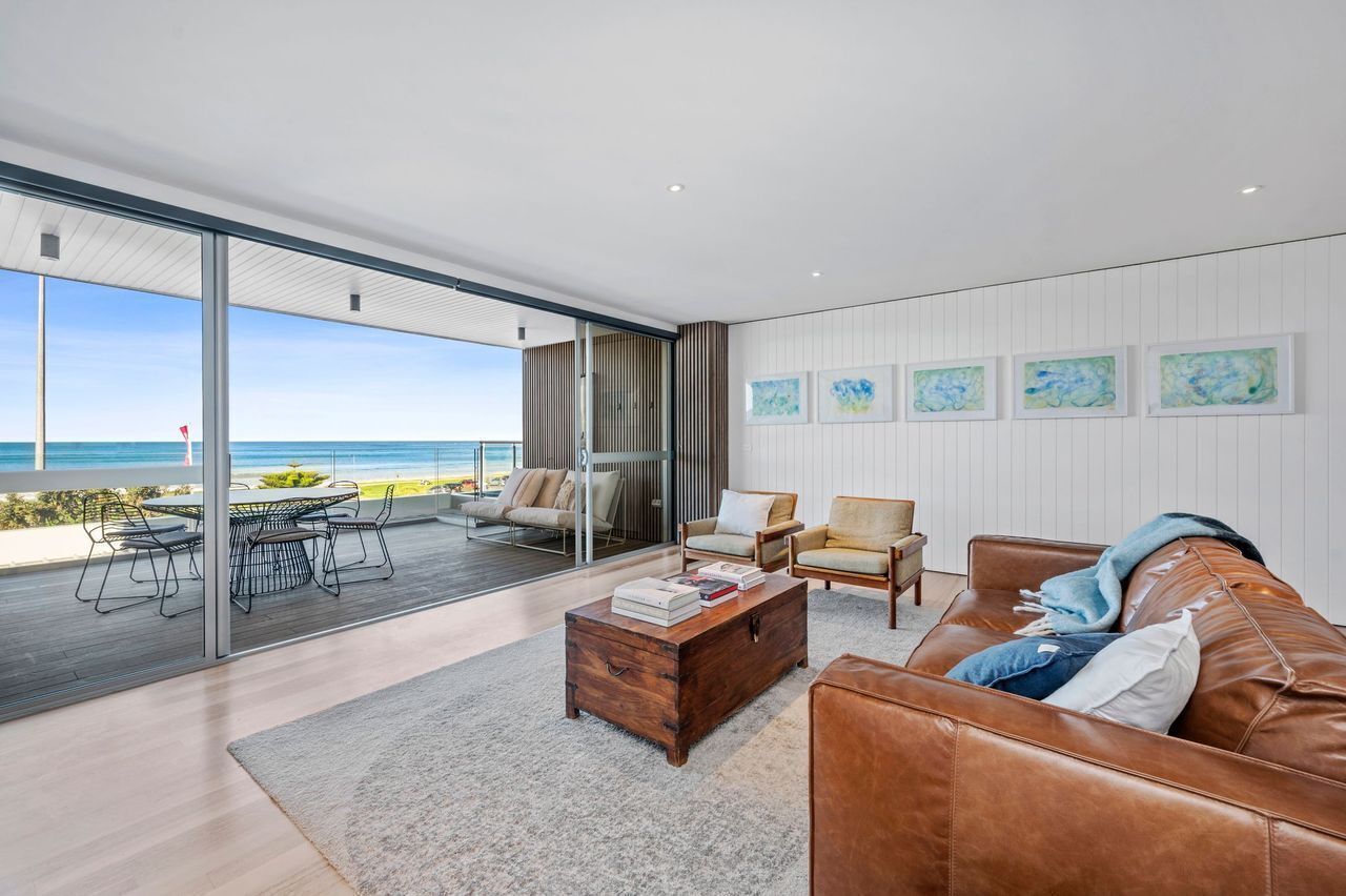 A modern living room with a large glass door leading to a balcony overlooking the sea.