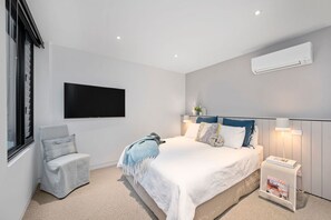 Ein modernes Schlafzimmer mit einem Bett, einem Sessel, einem Fernseher und einer Klimaanlage.