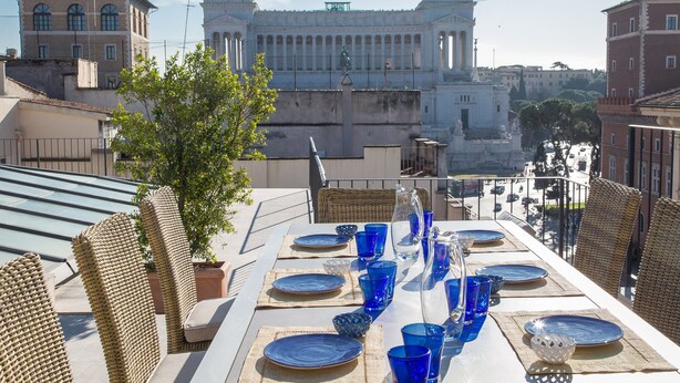 Un espace de restauration aménagé sur le toit, avec une table dressée pour quatre personnes, offrant une vue sur un bâtiment historique orné de statues.