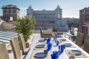 A rooftop dining area with a table set for four, overlooking a historic building with statues. - Amazing View Piazza Venezia (Rome)
