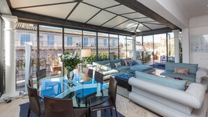 Un vaste espace de vie comprenant une table à manger en verre, des sièges confortables et une vue sur la ville.
