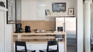 Une cuisine moderne avec un plan de travail en bois, deux chaises noires, un réfrigérateur en acier inoxydable et une machine à café.