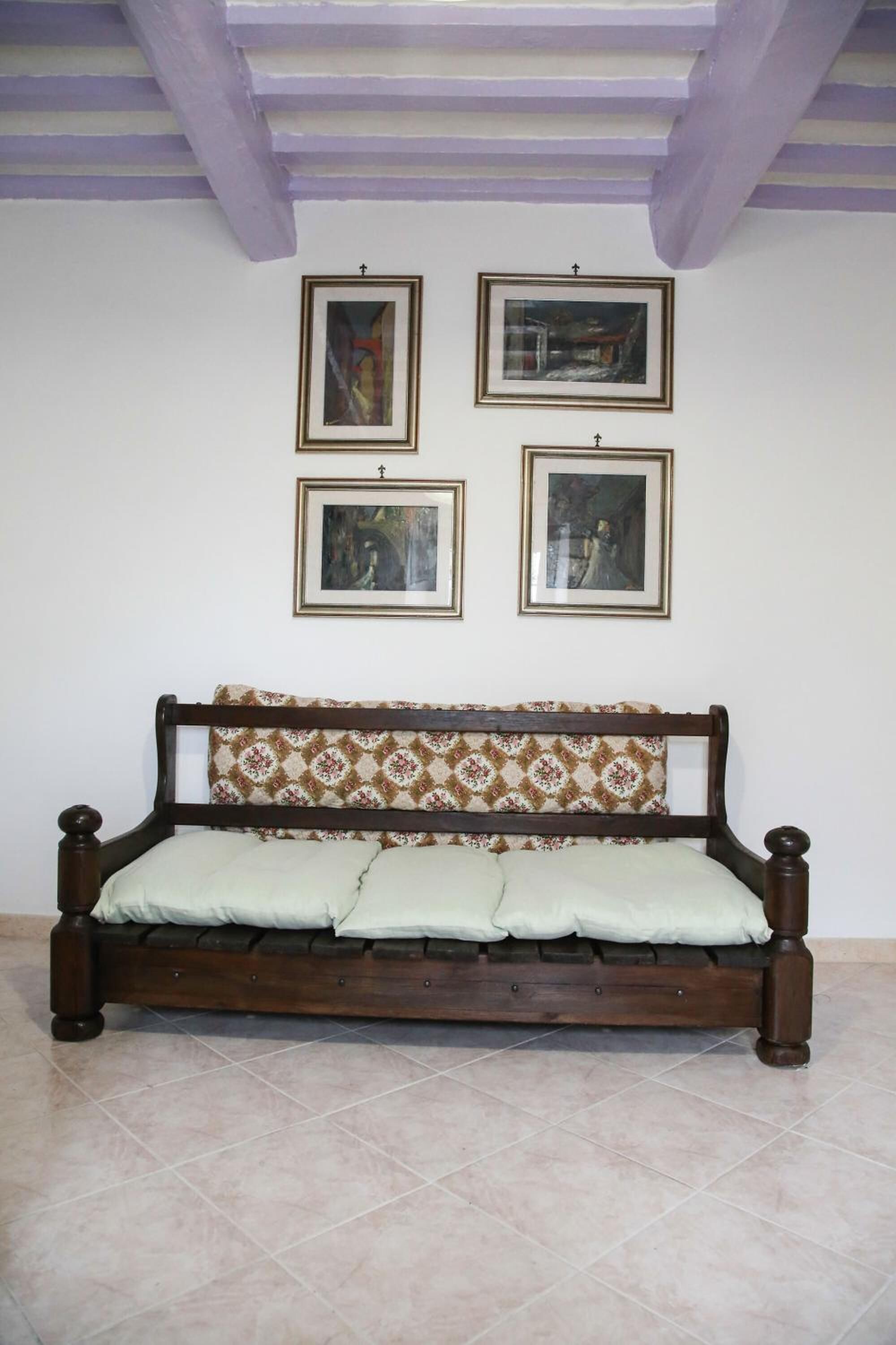 A room with a wooden bed, a patterned pillow, and four framed pictures on the wall.