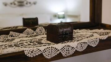 A small, ornate chest placed on a lace doily, with a mirror reflecting a lamp and a framed picture in the background.