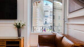 A room with a leather sofa, a flat-screen TV, a potted plant, and a window with a view of classical architecture. - Amazing Vittoriano (Rome)